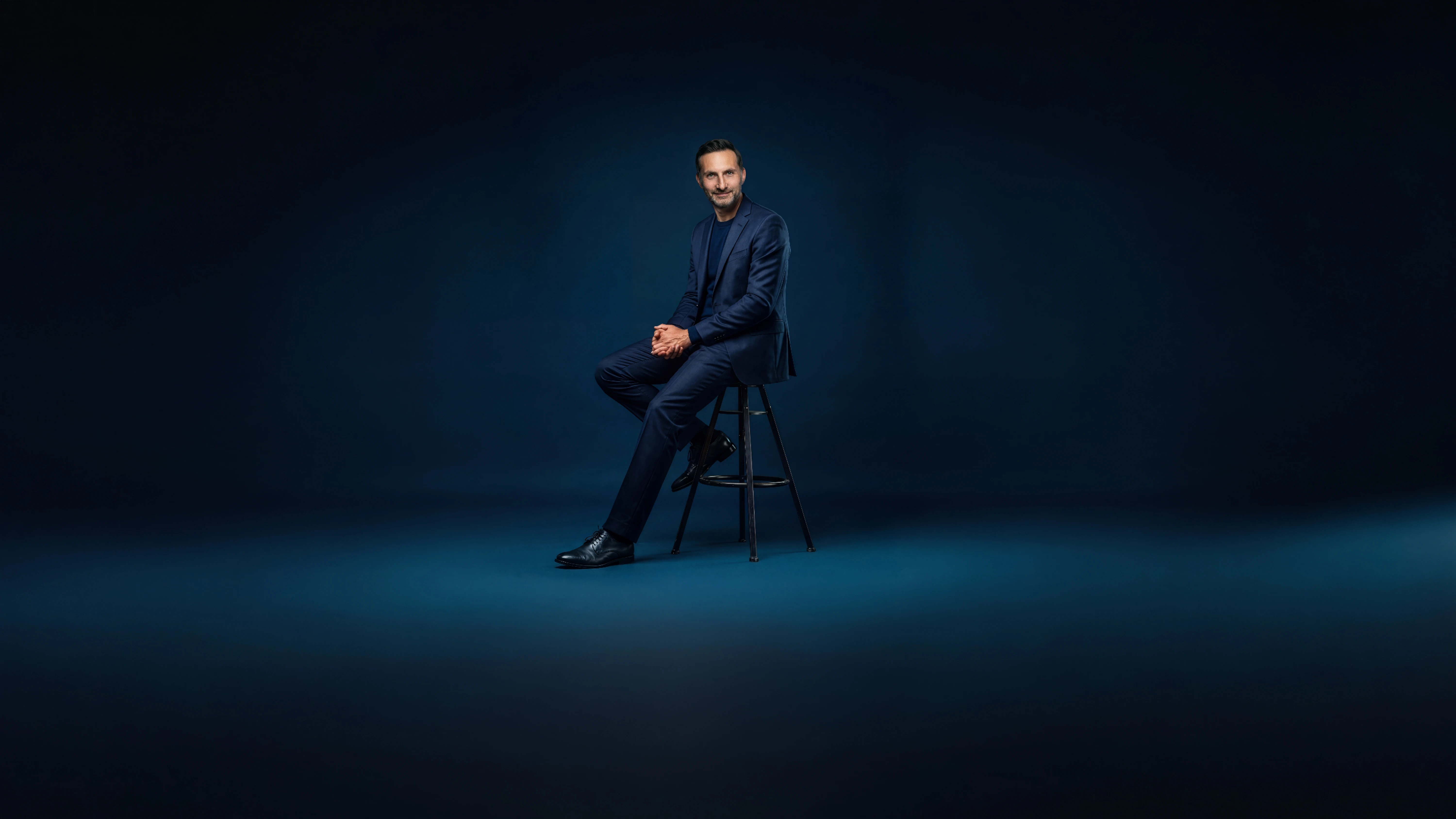Andrej Krahne sitting on a stool in a dark blue studio